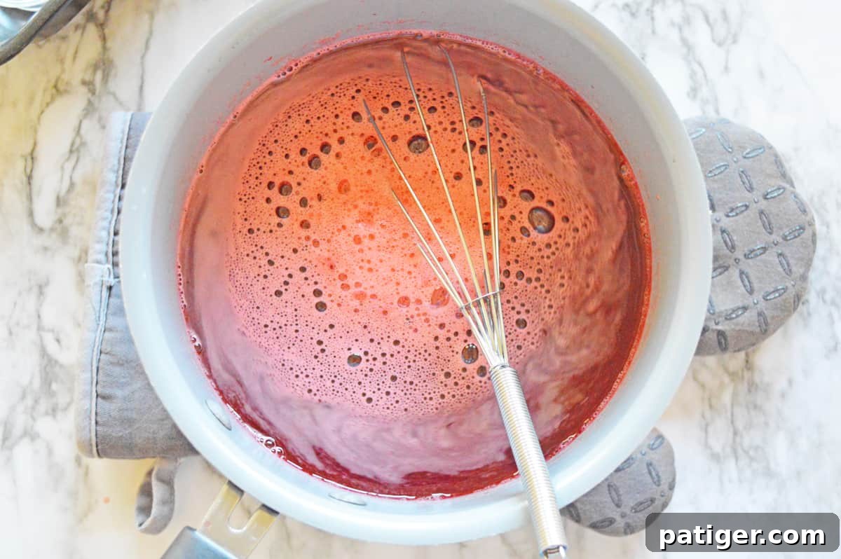 Bowl of strawberry jello shot mixture being whisked with a wire whisk to ensure full dissolution.