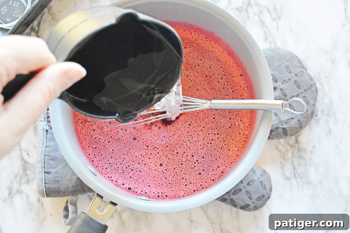 Vodka being carefully poured into a bowl of strawberry jello mixture, ready for chilling.
