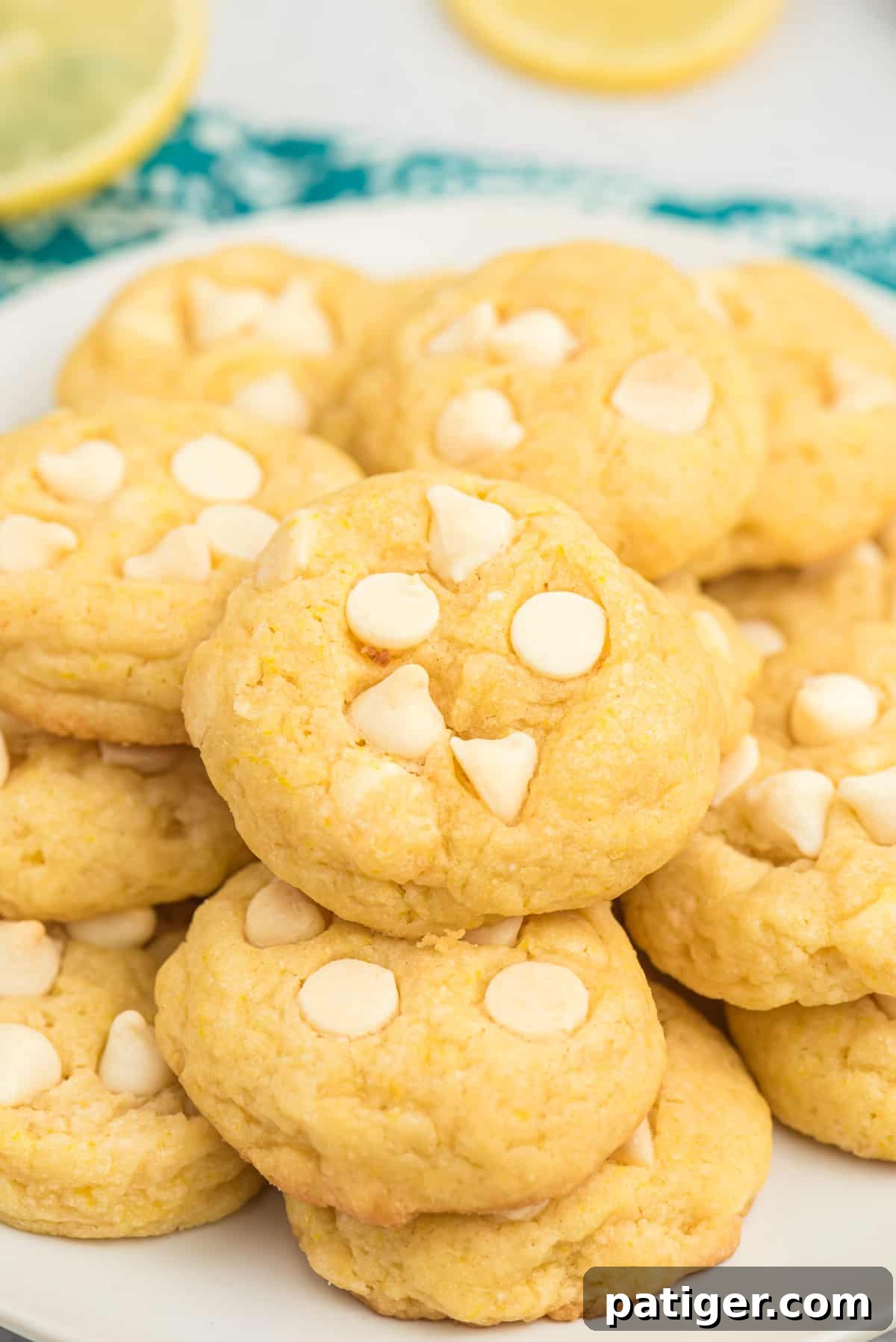 Lemon pudding cookies with white chocolate chips piled on serving plate, showcasing their soft texture and vibrant color.