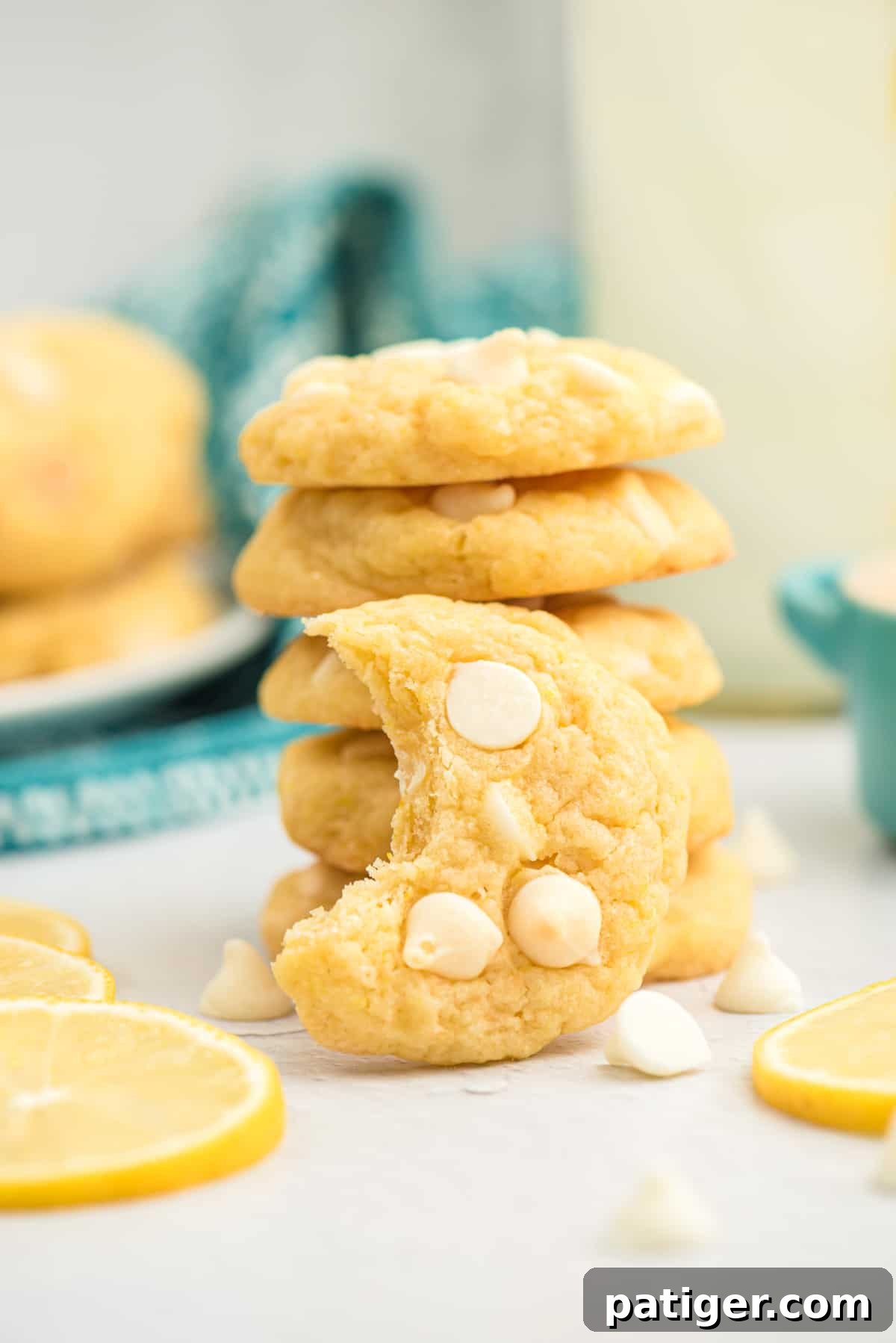 Stacked lemon cookies with white chocolate chips, one with a bite taken out, highlighting their soft, inviting texture.