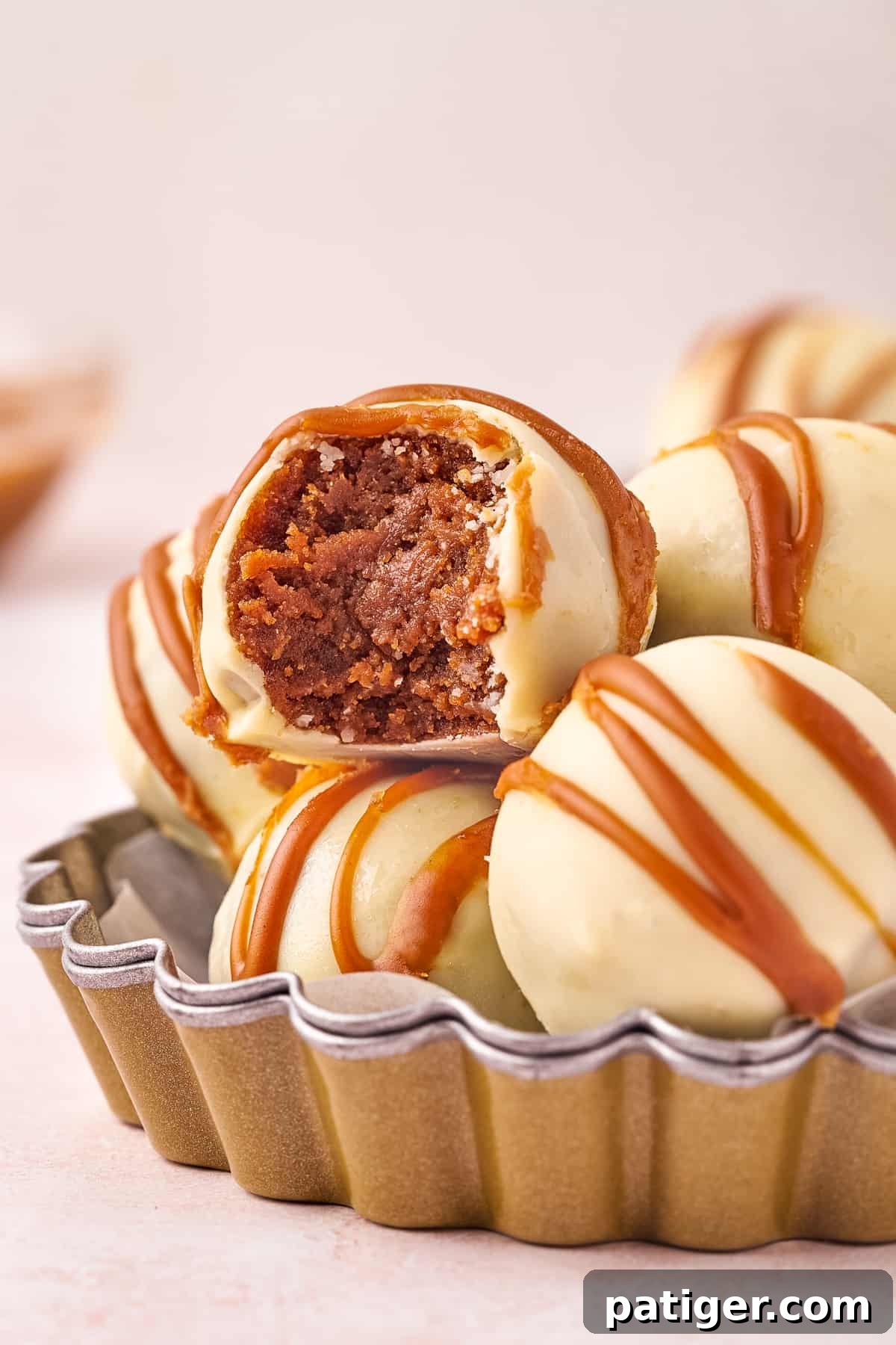 Decadent No-Bake Biscoff Truffles made with crushed Biscoff cookies, cookie butter, and cream cheese, coated in smooth white chocolate. One truffle shows a tempting bite taken out.