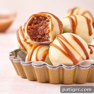 Biscoff Truffles made with crushed Biscoff cookies, cookie butter, and cream cheese with a white chocolate coating. One of the truffles has a bite taken out of it.