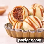 Biscoff Truffles made with crushed Biscoff cookies, cookie butter, and cream cheese with a white chocolate coating. One of the truffles has a bite taken out of it.