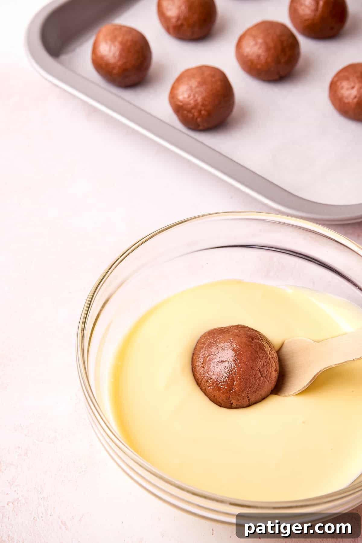 A Biscoff cookie truffle being carefully dipped into a bowl of melted white chocolate, ensuring an even coating.