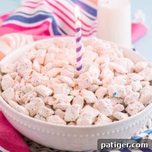 Large white bowl of funfetti puppy chow with purple birthday candle in the center and a glass of milk, colorful paper straws, sprinkles, and a colorful linen in background.