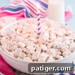Large white bowl of funfetti puppy chow with purple birthday candle in the center and a glass of milk, colorful paper straws, sprinkles, and a colorful linen in background.