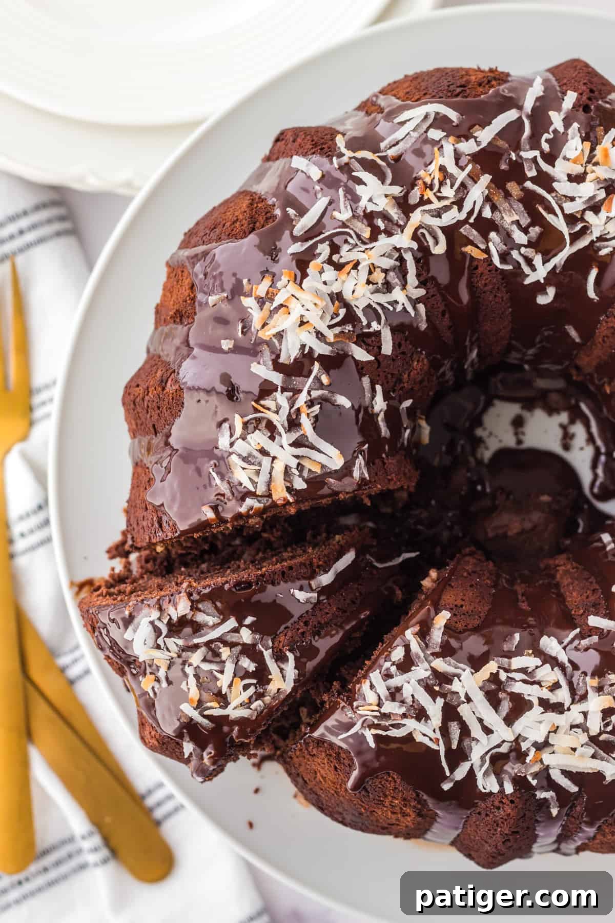 Chocolate coconut bundt cake with chocolate ganache and toasted coconut with a single slice cut out.