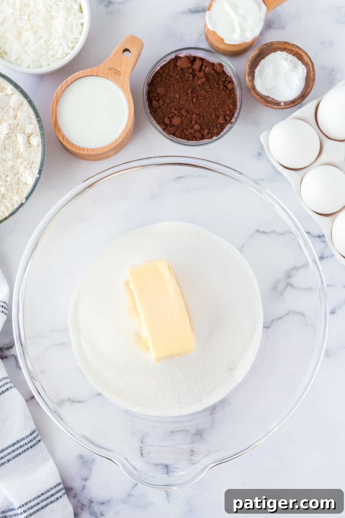 Butter and sugar in large glass mixing bowl, surrounded by other ingredients.