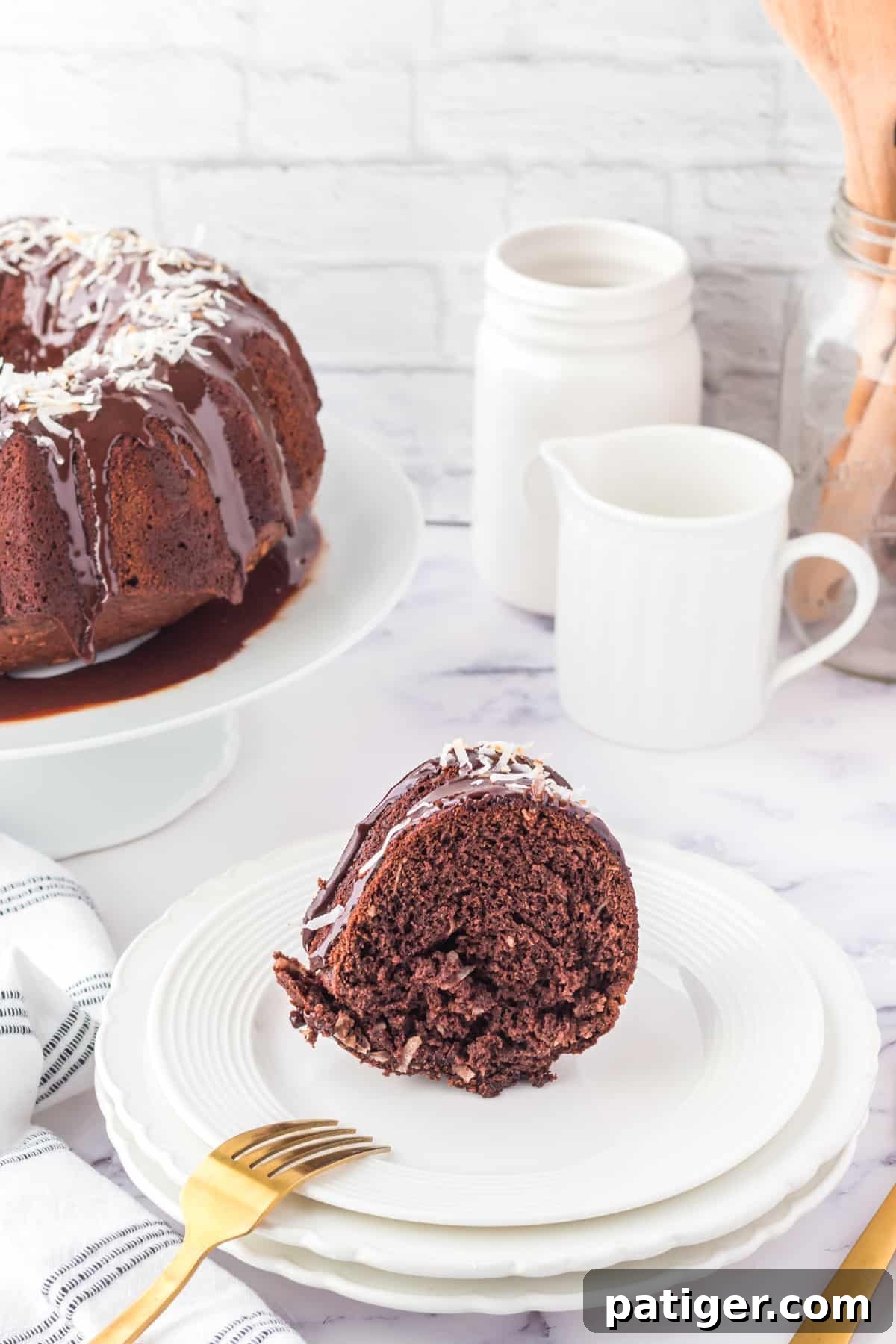 Slice of Chocolate Coconut Cake on white plate with remaining Bundt cake on a cake stand in the background.