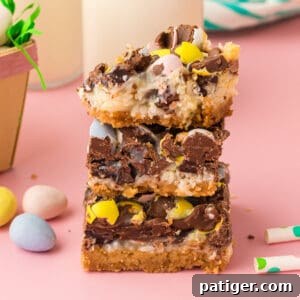 Easter dessert bars with sweetened condensed milk, chocolate chips, coconut, and chocolate eggs stacked on top of one another with top bar missing a bite.