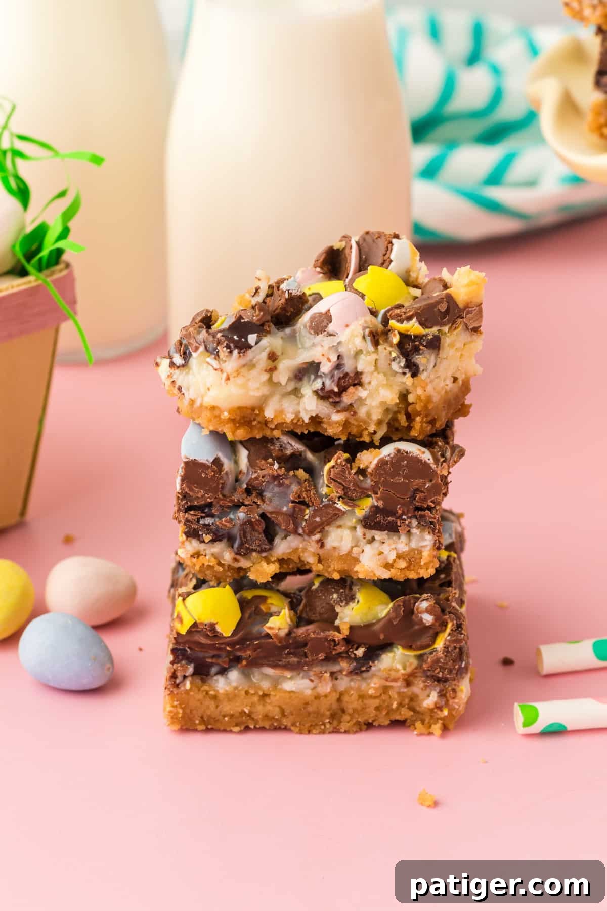 Easter dessert bars with sweetened condensed milk, chocolate chips, coconut, and chocolate eggs stacked on top of one another with top bar missing a bite.