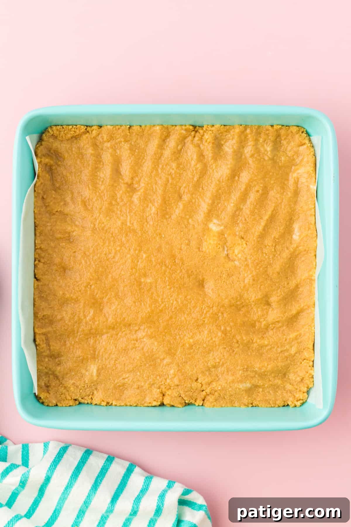 Golden oreo cookie crust pressed into light blue square baking pan.
