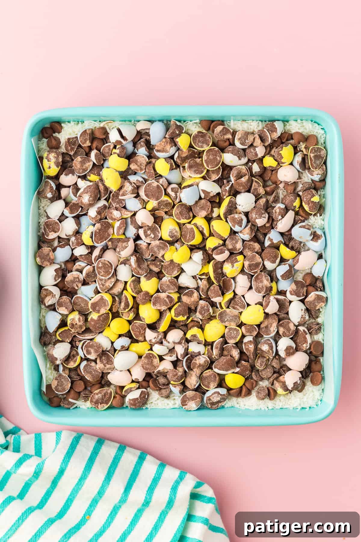 Crushed mini eggs on top of chocolate chips and shredded coconut in square baking pan.