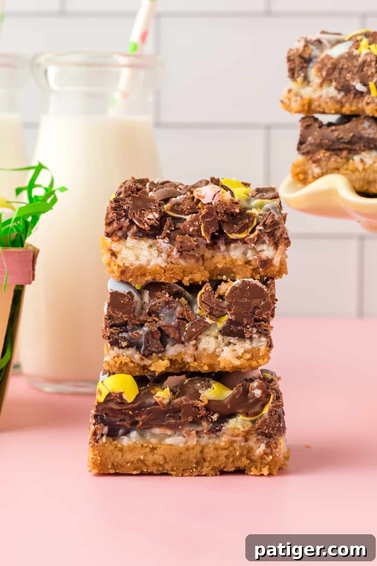 Three thick easter dessert bars stacked on top of one another with glass of milk and additional bars in the background.