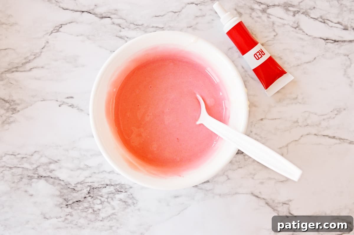 red cupcake batter in bowl with spoon and gel food coloring tube.