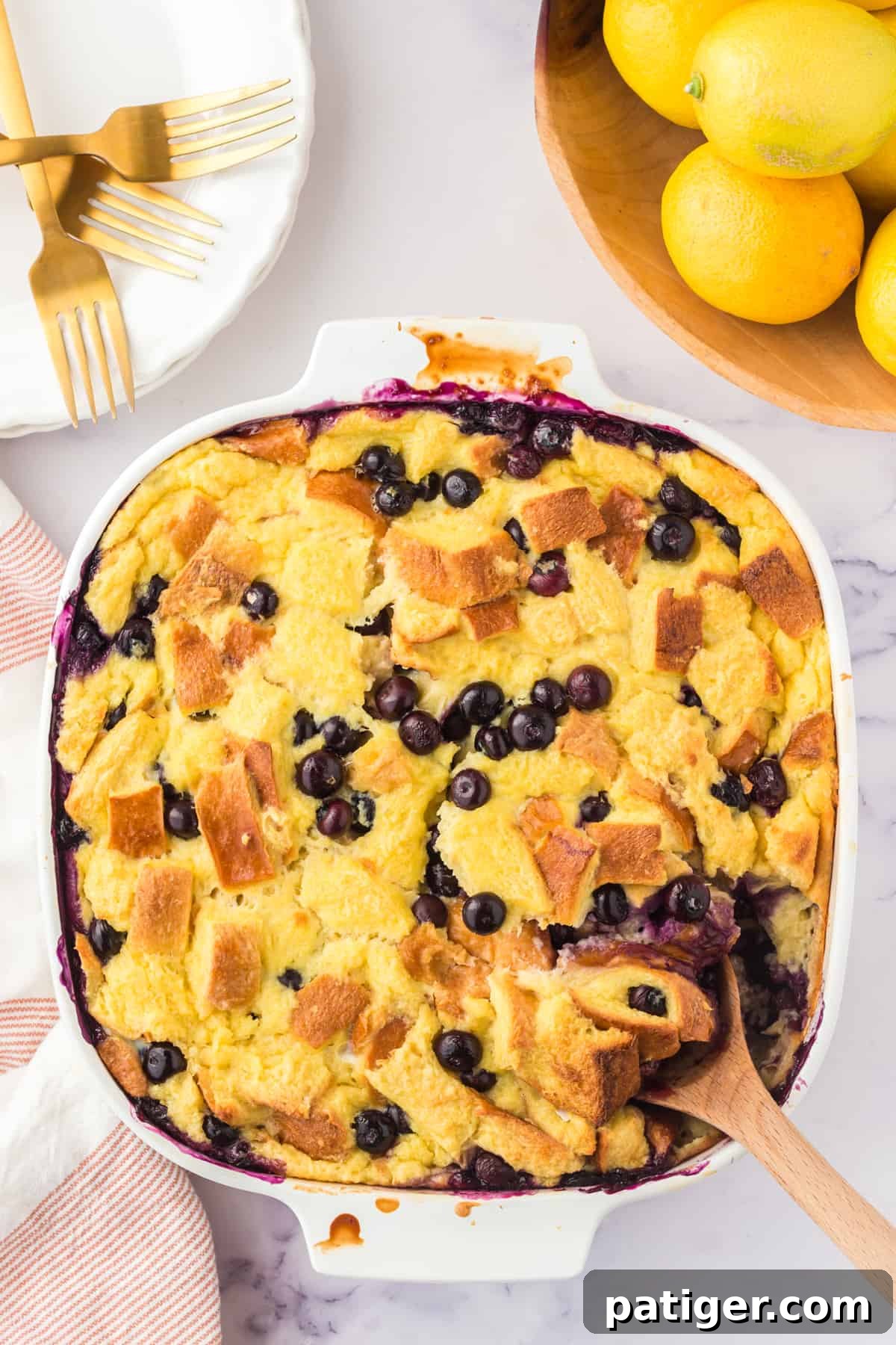 Lemon blueberry bread pudding in an square baking dish with wooden spoon sticking out of the corner.