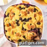 Lemon blueberry bread pudding in an square baking dish with wooden spoon sticking out of the corner.