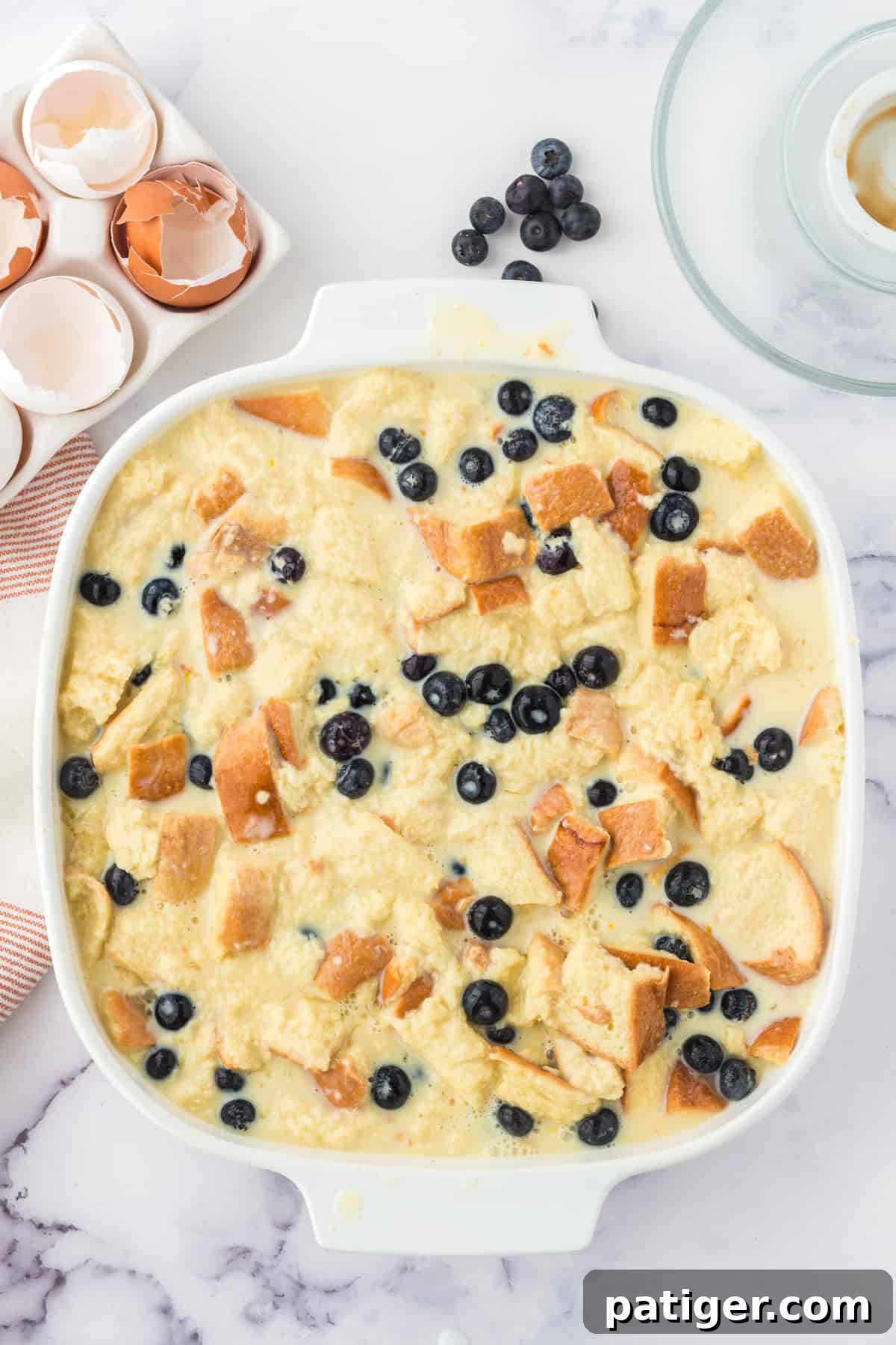 Unbaked lemon blueberry bread pudding in square casserole dish.