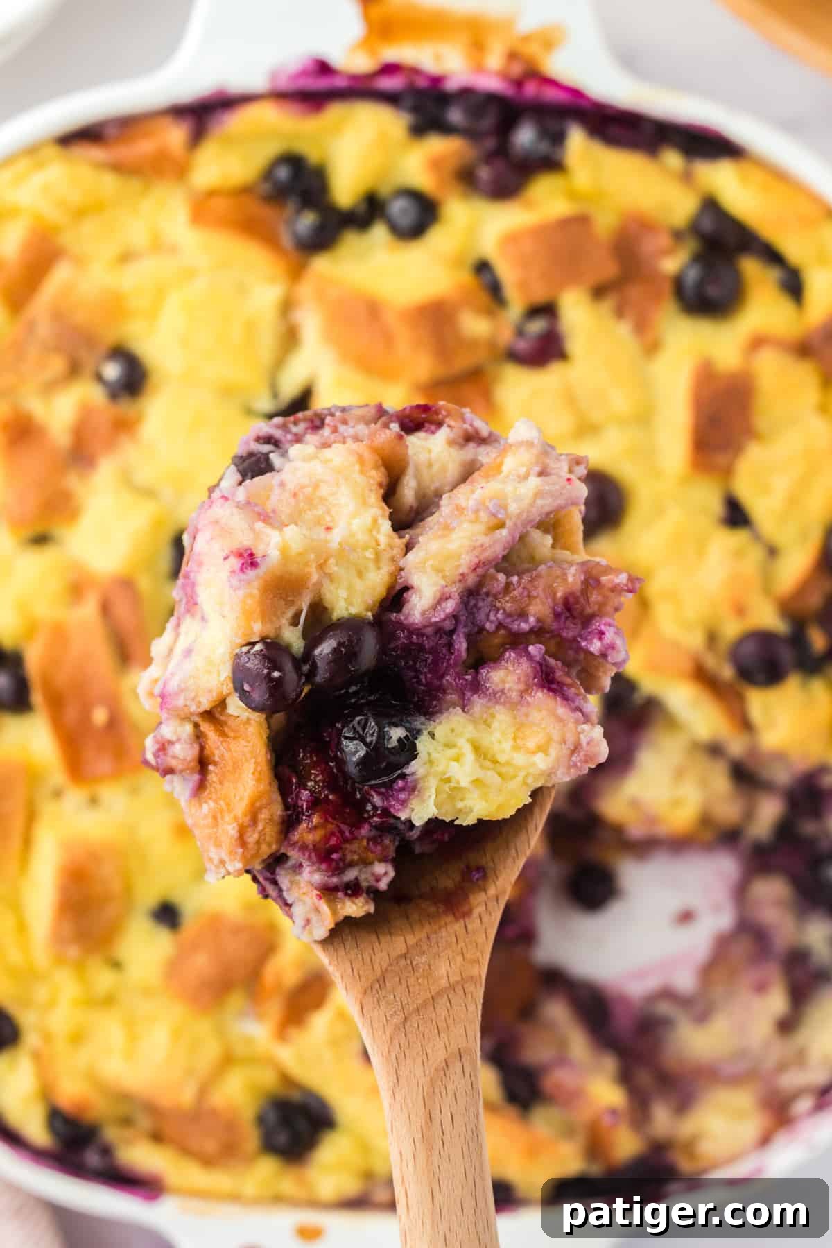 Wooden serving spoon lifting a spoonful of bread pudding out of the dish.