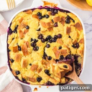 Lemon blueberry bread pudding in an square baking dish with wooden spoon sticking out of the corner.
