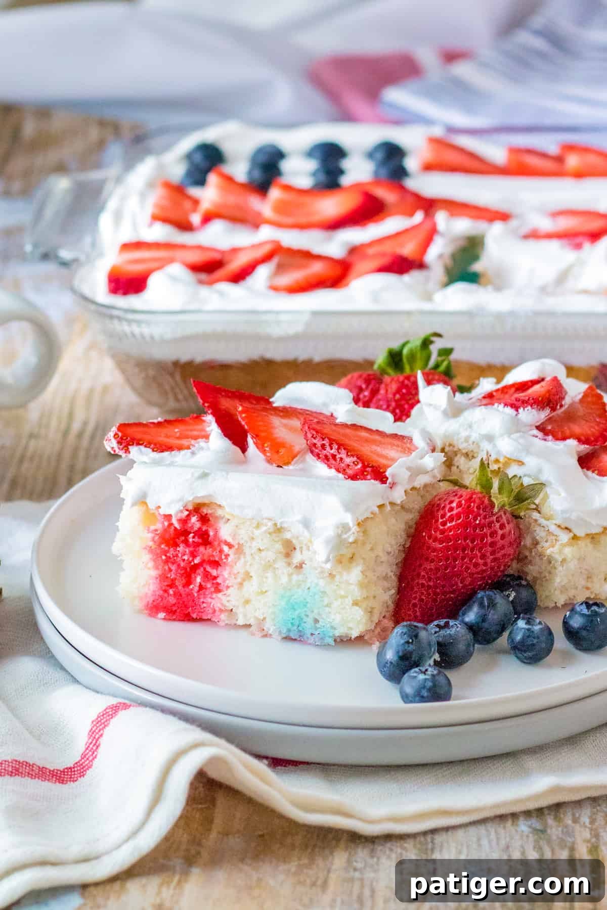 4th of July poke cake with red and blue jello, cool whip topping, and fresh berries in the shape of a flag on top.