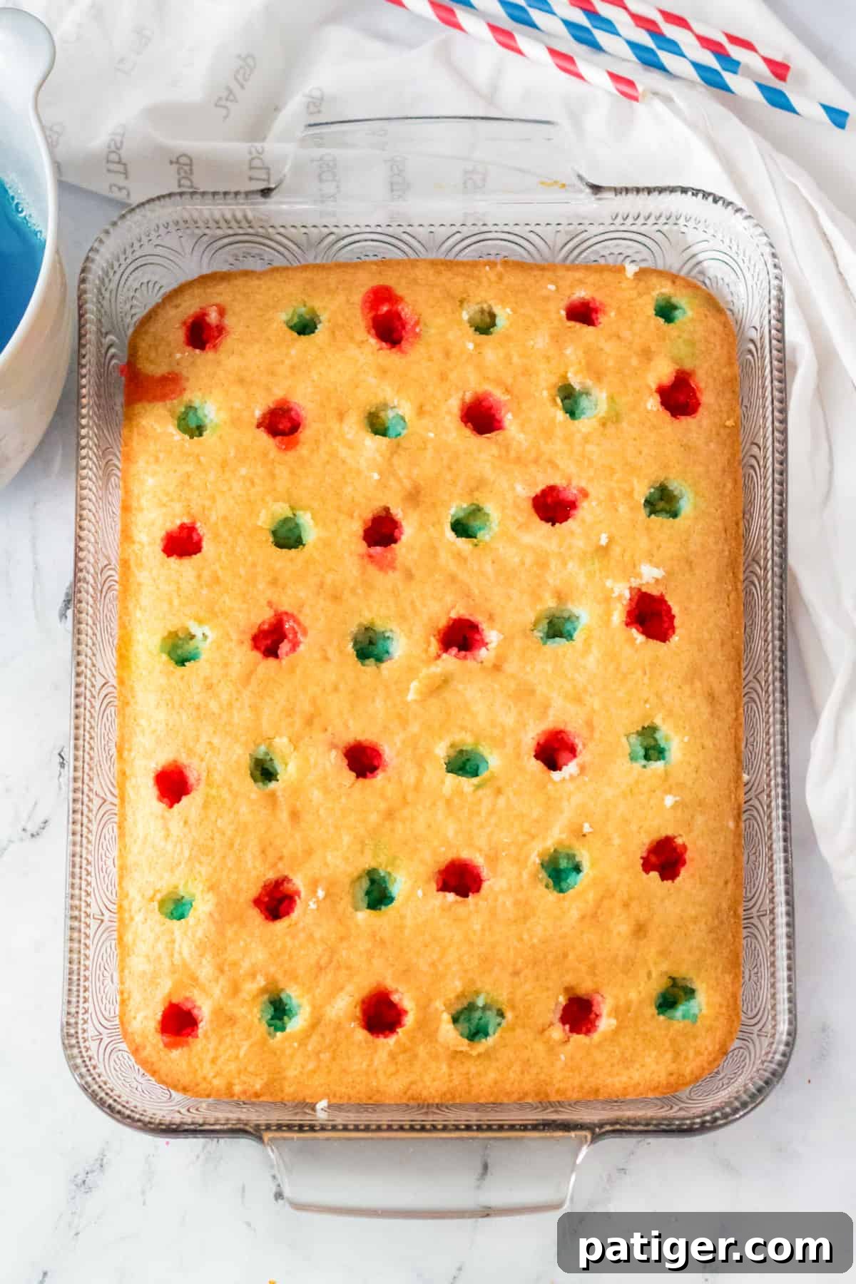 Golden cake with holes poked throughout the top and red and blue jello poured into alternating holes.
