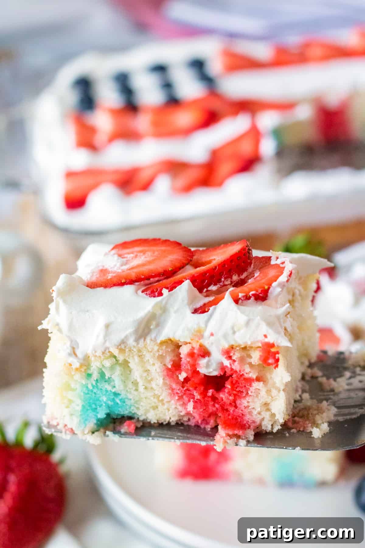 A piece of patriotic poke cake being lifted out of the cake to be served.