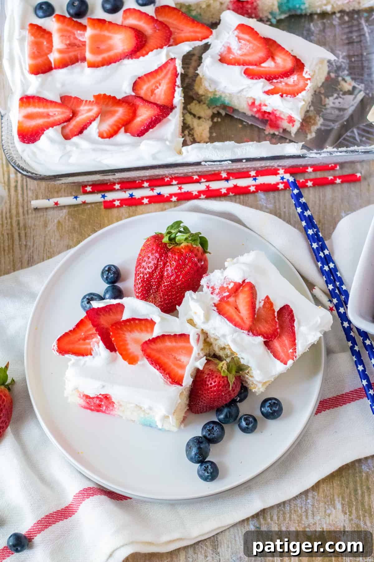 4th of July flag cake topped with fresh fruit. Two slices are removed and placed on plate with fresh berries.