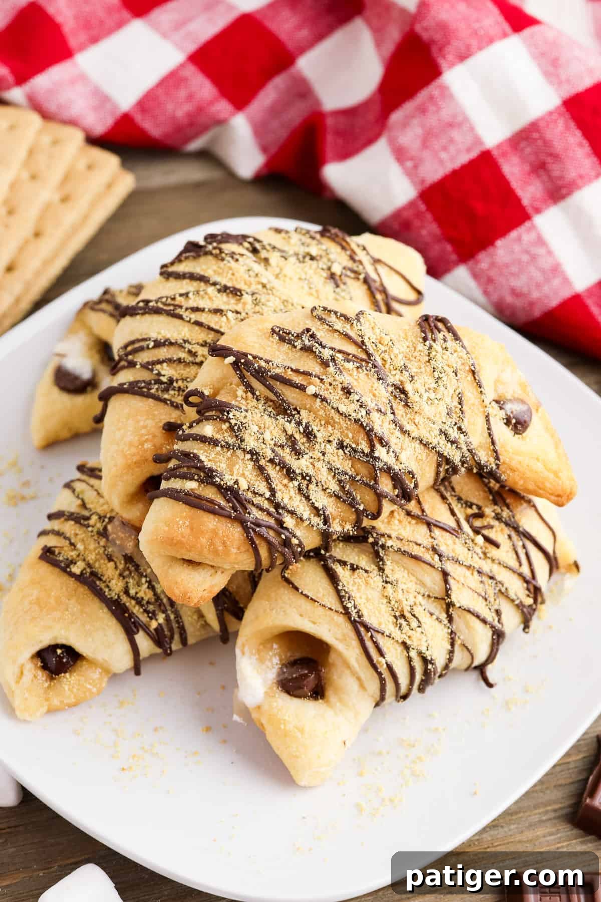 Golden brown S'mores crescent rolls drizzled with melted chocolate and sprinkled with graham cracker crumbs, served on a white plate.