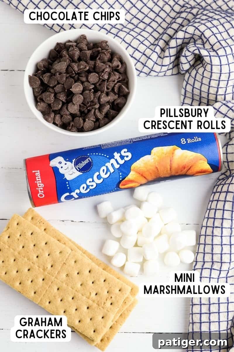 A roll of Pillsbury crescent roll dough, a bowl of chocolate chips, a bowl of mini marshmallows, and whole graham crackers laid out on a wooden cutting board.