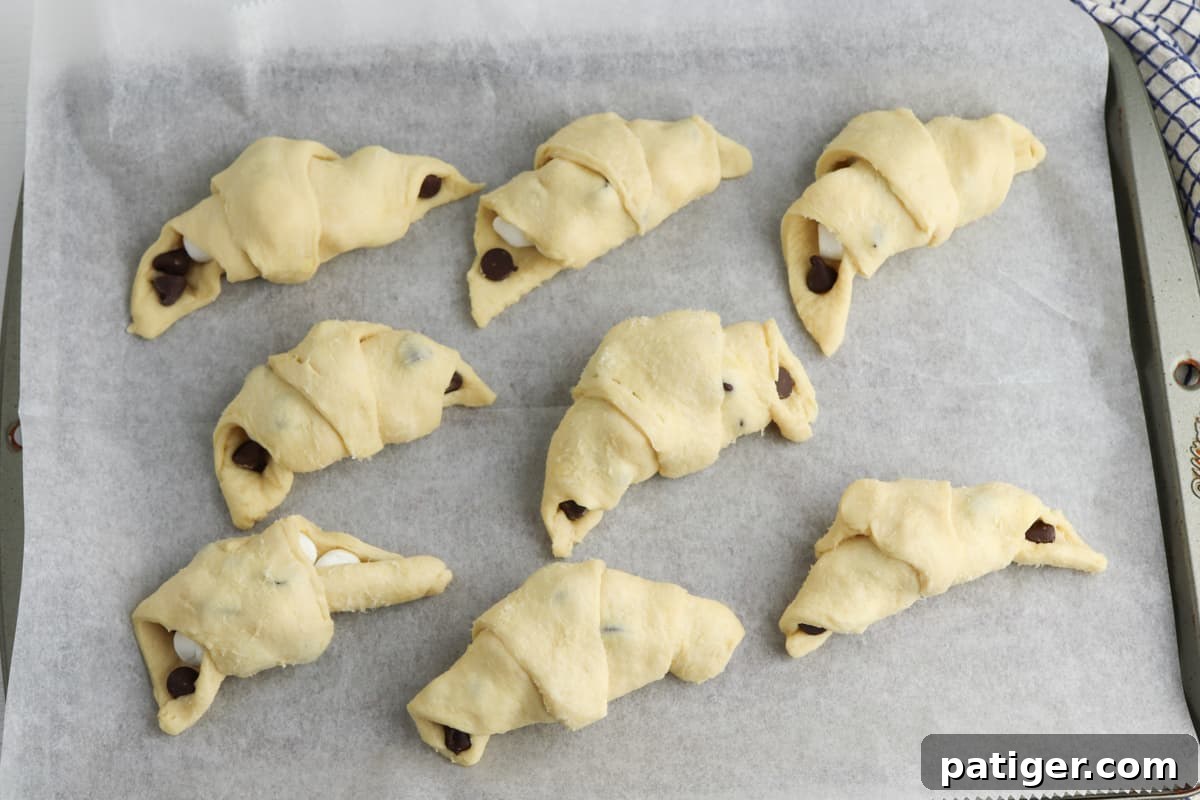 Several s'mores crescent roll ups, already rolled and filled, arranged neatly on a parchment-lined baking sheet, ready for baking.