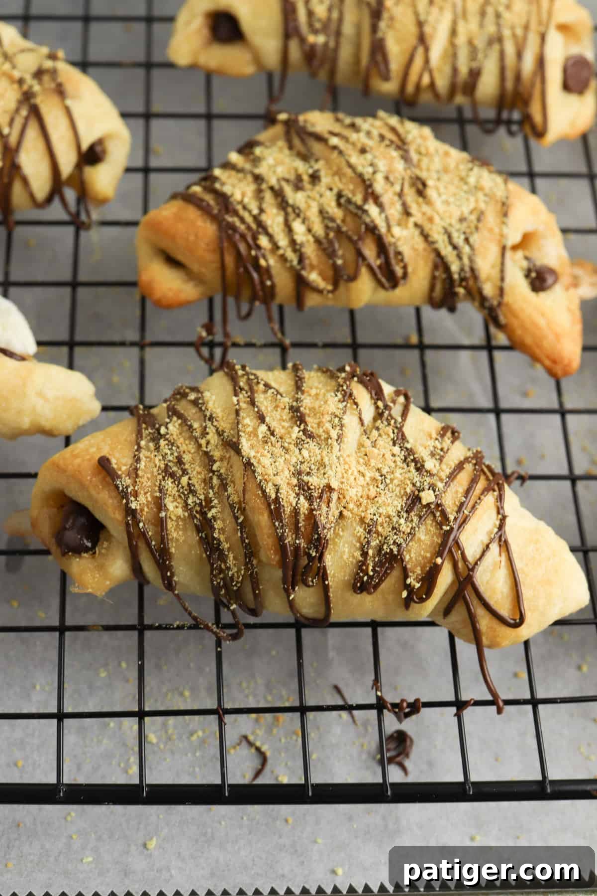 Freshly baked S'mores crescent rolls cooling on a wire rack, ready for the final chocolate drizzle and graham cracker crumb topping.