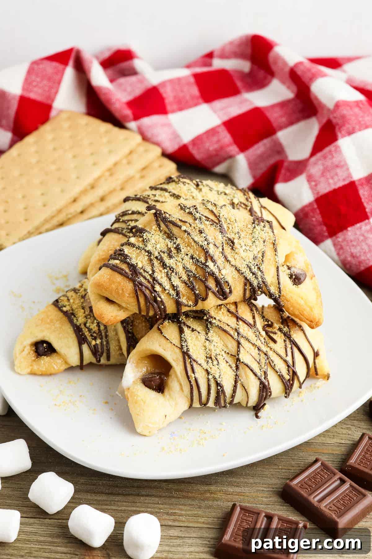 A s'mores crescent roll on a white plate, surrounded by whole graham crackers, mini marshmallows, and chocolate chips, ready to be enjoyed.
