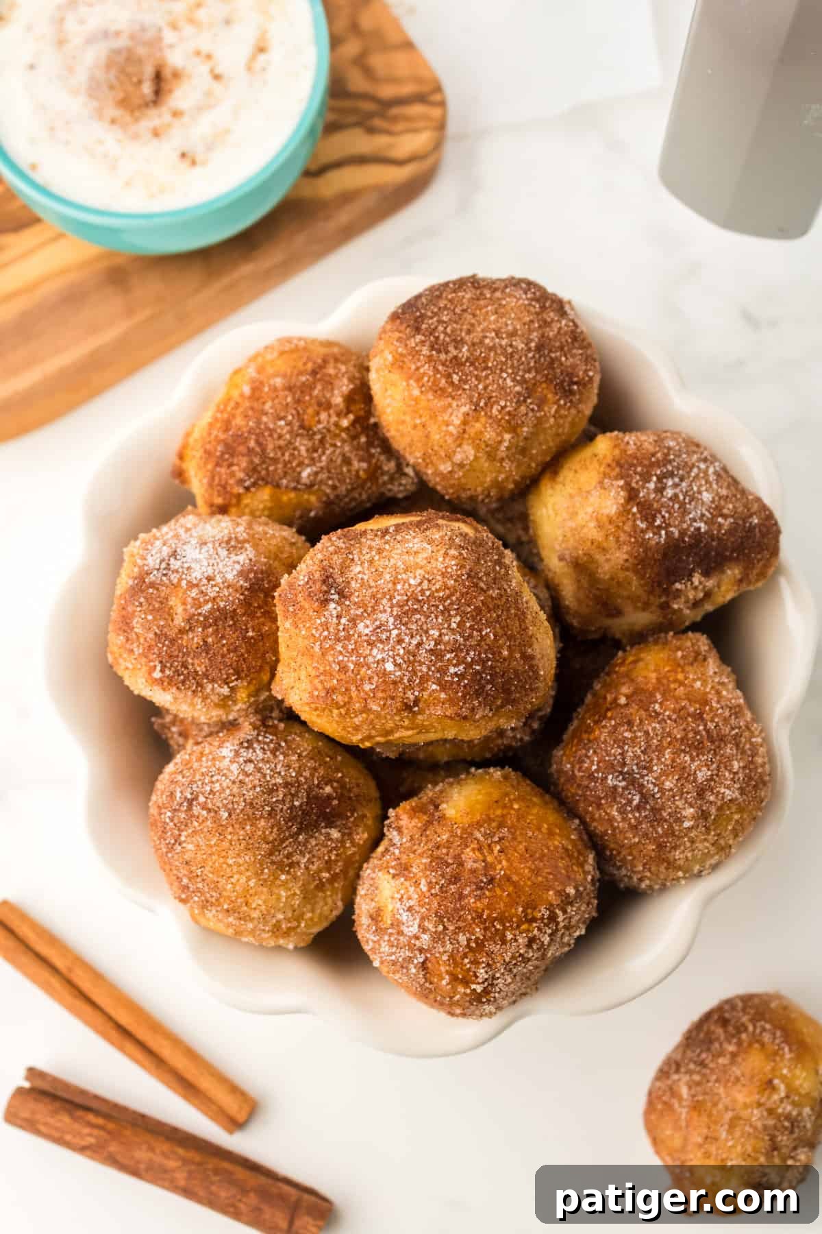 A white bowl filled with golden brown air fryer cinnamon sugar pretzel bites, with a creamy dipping sauce in the background.