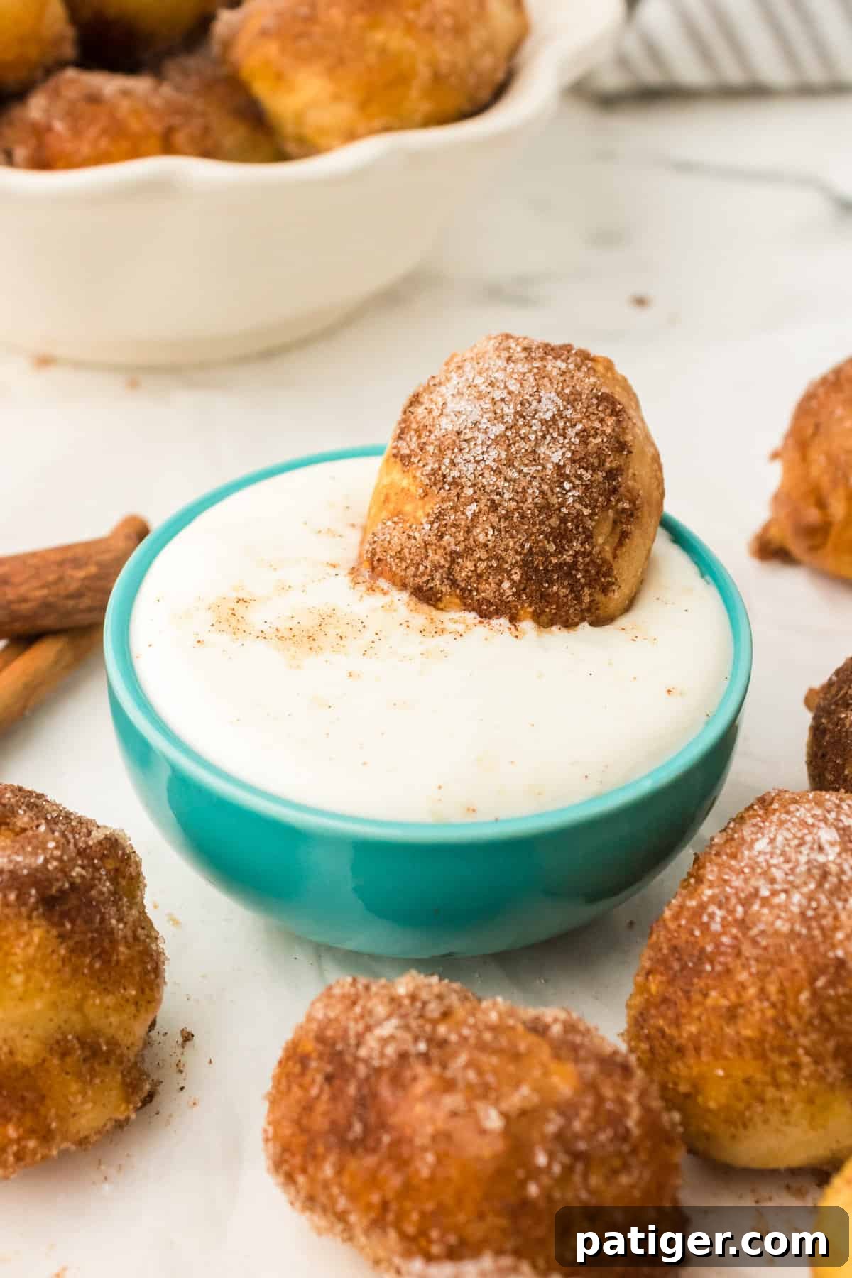Close-up of a single cinnamon pretzel bite dipped into a creamy white sauce, highlighting its sweet coating and soft texture.