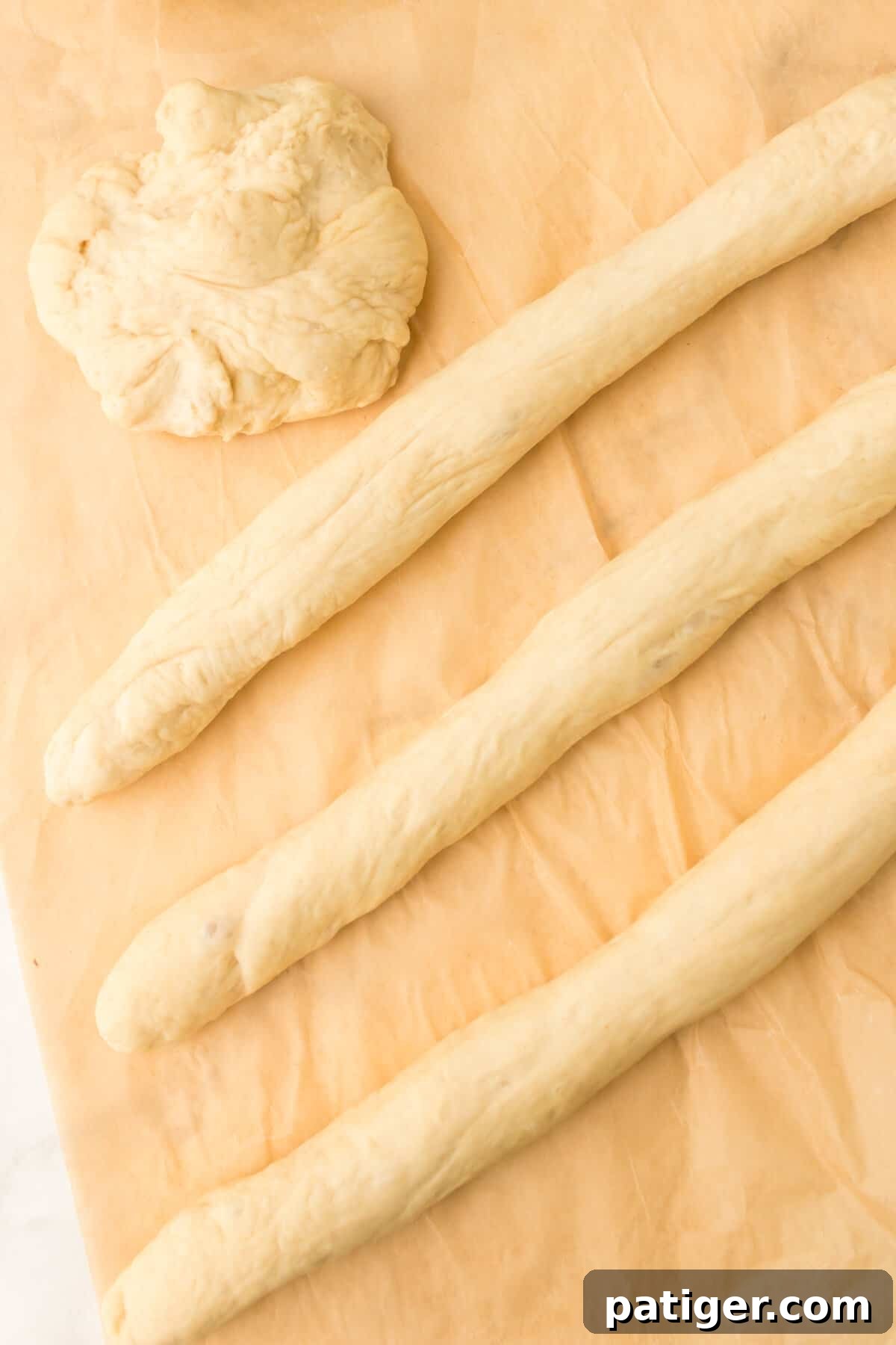 Pizza dough divided into four sections and rolled into long, even ropes on a cutting board, ready for cutting into bites.