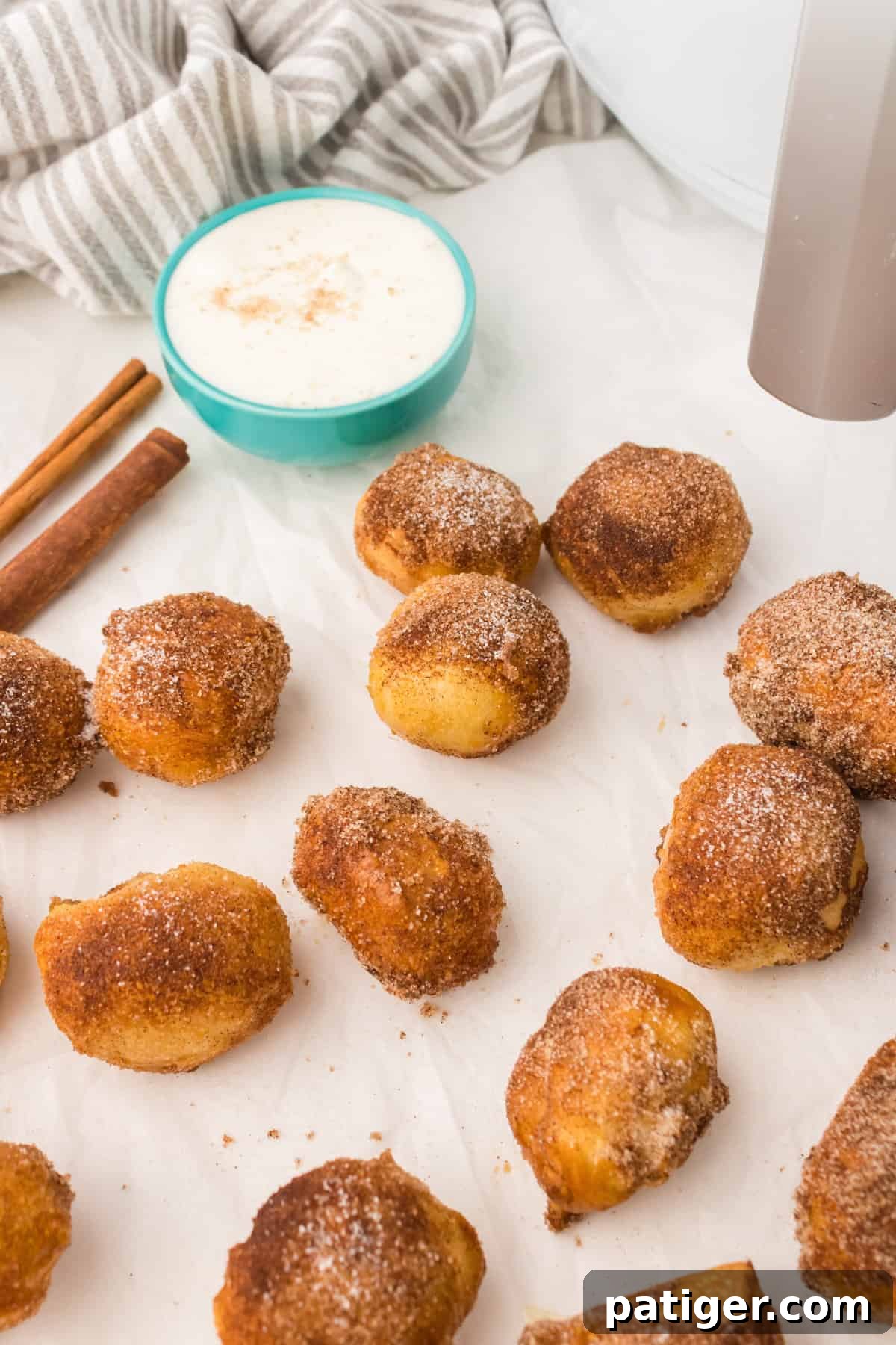 Freshly made cinnamon sugar covered pretzel bites arranged on parchment paper, with a bowl of dipping sauce blurred in the background.