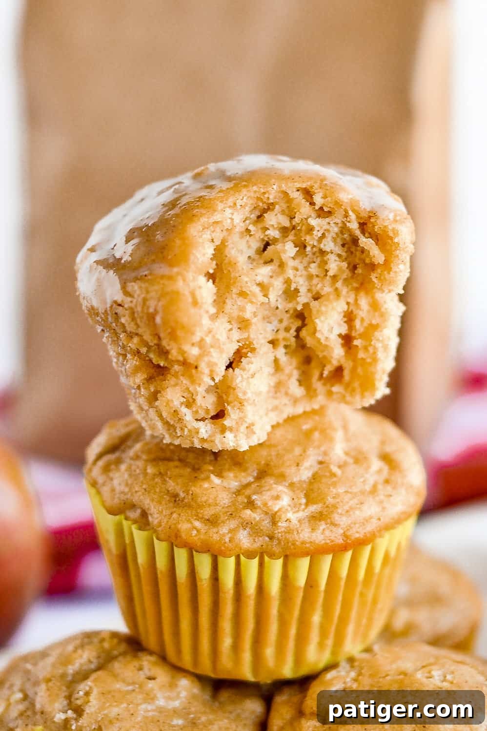 A close-up of a perfectly baked apple muffin with a bite taken out, revealing its moist, tender, and fluffy interior, flecked with pieces of apple and oats.
