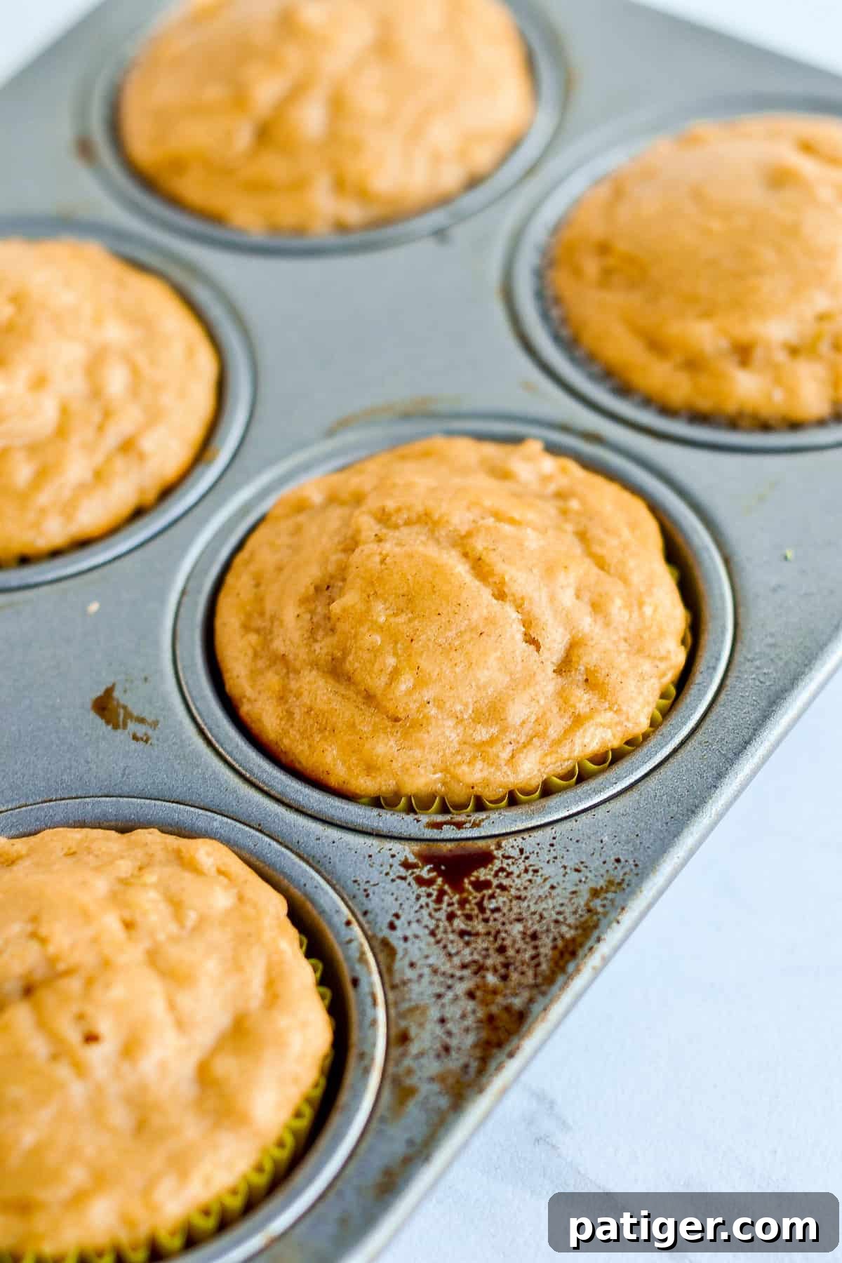 Freshly baked apple spice muffins nestled in a muffin tin, their golden-brown tops hinting at the warmth and flavor within.