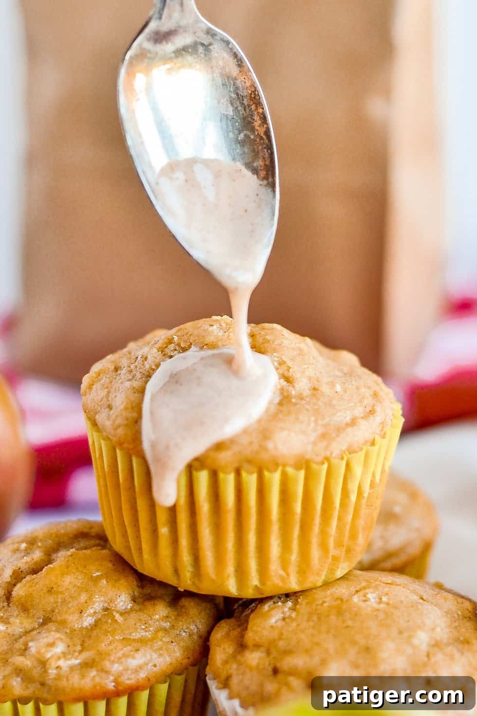 A delectable apple muffin receiving a generous drizzle of sweet cinnamon glaze, enhancing its appeal and flavor.