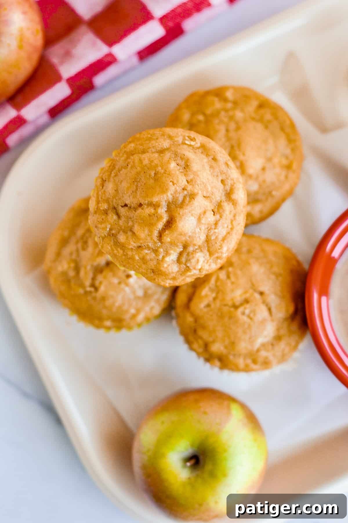 A lunch tray featuring golden-brown apple oat muffins alongside a fresh, crisp red apple, ready for a wholesome meal.