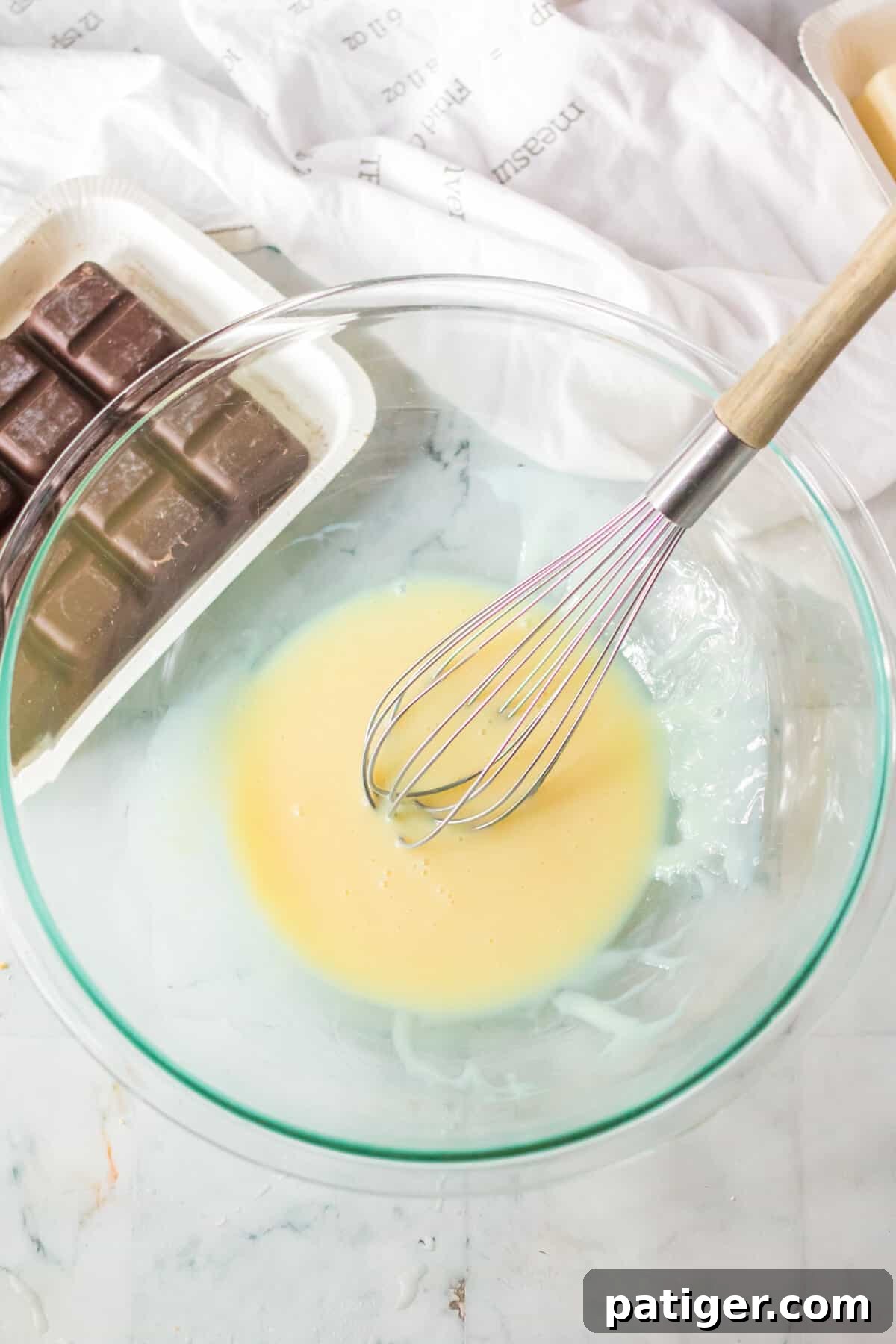 Sweetened condensed milk and peppermint extract are thoroughly combined in a clear glass mixing bowl using a wire whisk, creating the base for the peppermint filling.
