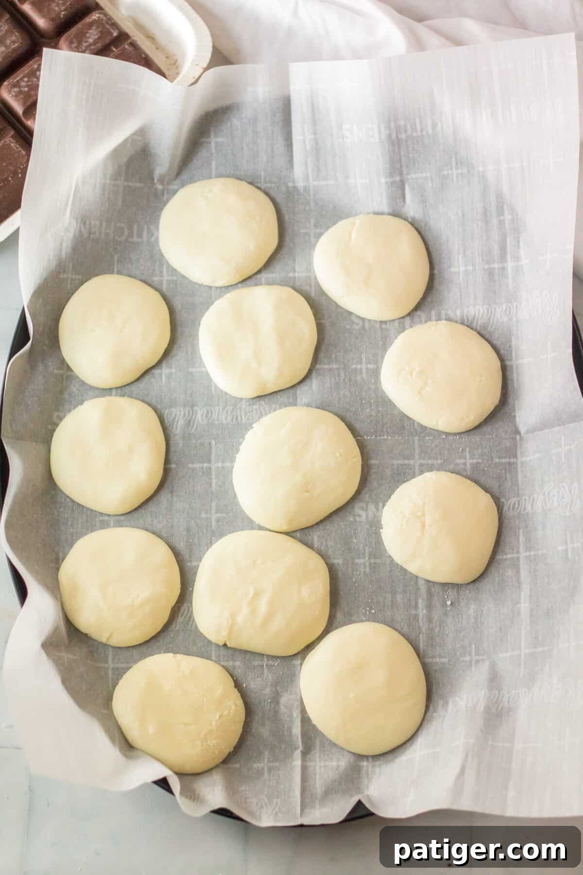 Uniform peppermint patty fillings, shaped into neat discs, are carefully arranged on a parchment-lined baking pan, prepared for chilling.