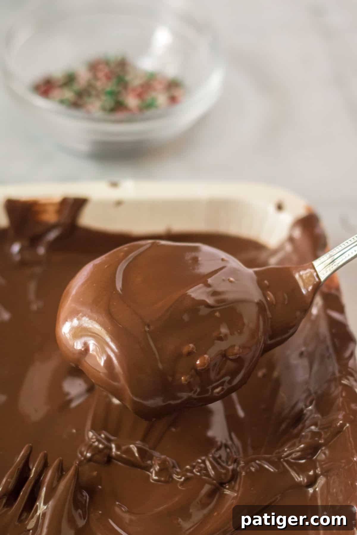 A homemade peppermint patty is carefully dipped into a bowl of glistening melted chocolate, ensuring a full and even coating.