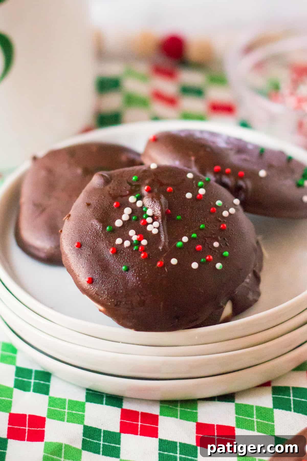 Several homemade chocolate mint candies, beautifully coated and topped with festive Christmas sprinkles, are artfully arranged on a pristine white plate.