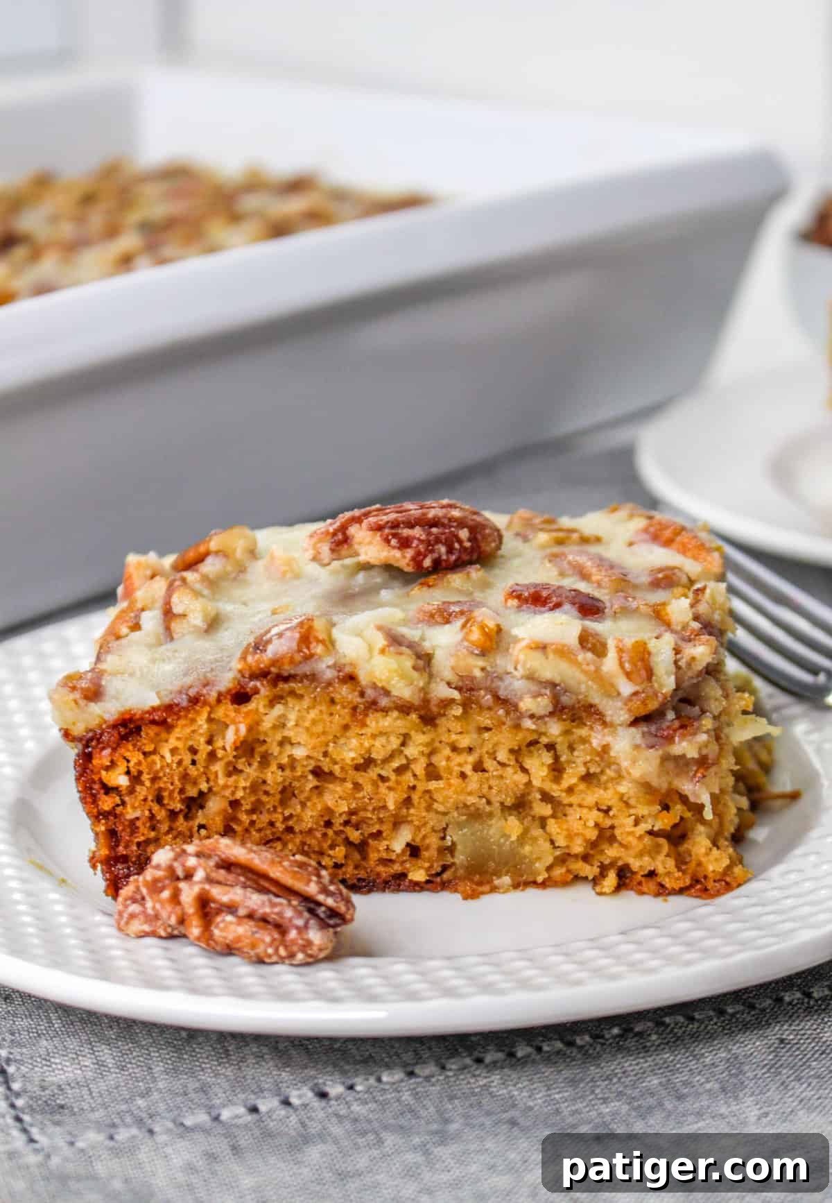 Fruit cocktail cake slice on a white plate with a pecan on top and pecan beside it.