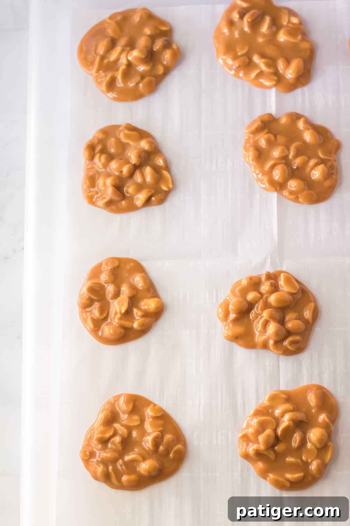 Tablespoon-sized mounds of caramel and peanut mixture cooling on parchment paper on a baking sheet.