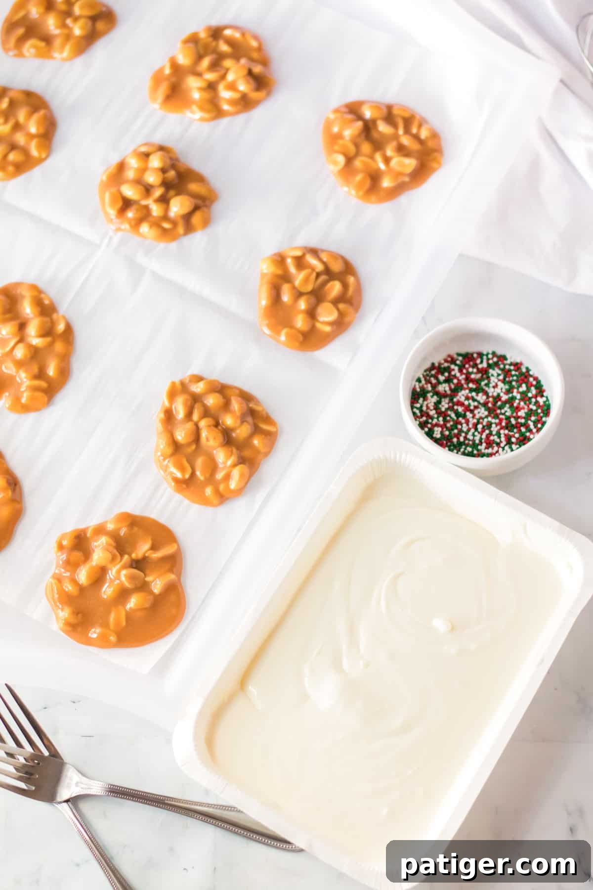 Melted white almond bark in a disposable tray, with set caramel peanut clusters and sprinkles nearby.