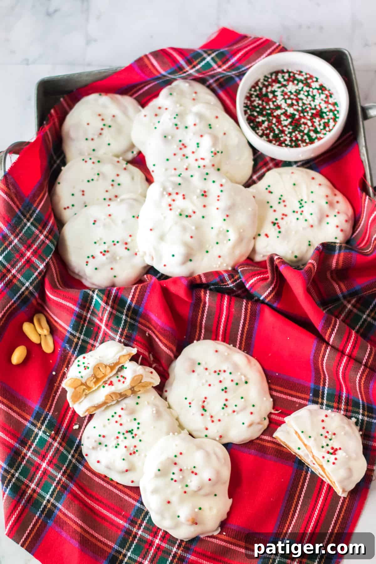 A festive rectangular tin filled with Polar Bear Paws candy, accompanied by a bowl of colorful Christmas sprinkles. Additional candies are scattered on a red plaid cloth.