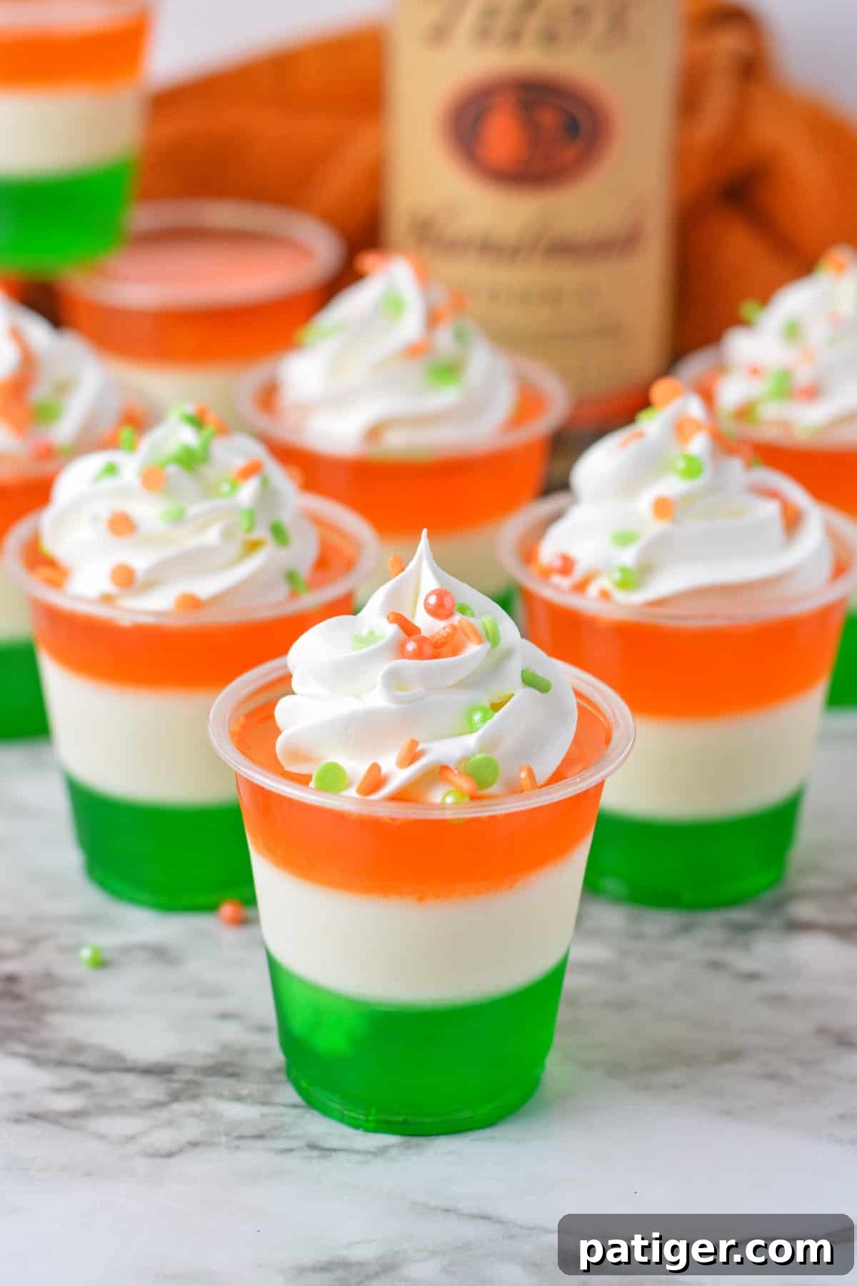 Green, white, and orange layered jello shots with whipped cream and sprinkles.